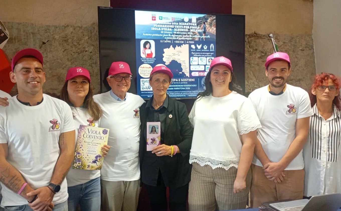 Foto di gruppo con i cappellini rosa davanti allo schermo con il programma della maratona Uniti per Paolo
